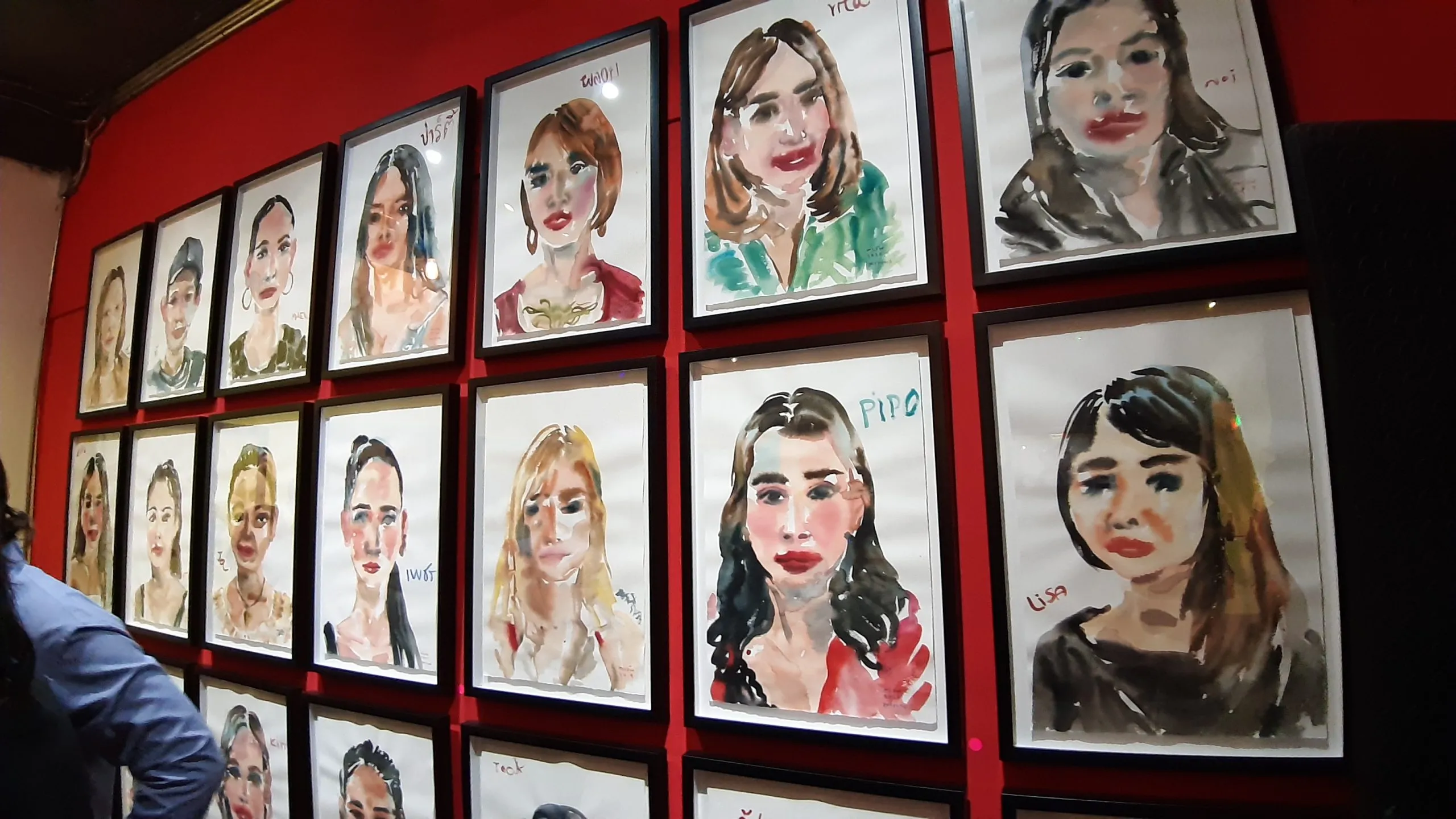 A wall of watercolour portraits of Patpong night workers, hung salon-style at the Patpong Museum.